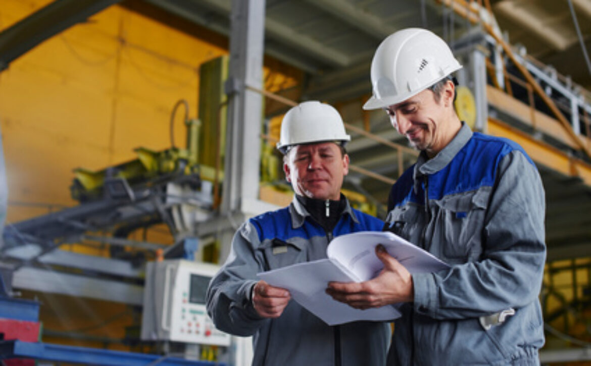 Two workers in overalls holding documents and looking at them in the premises of the factory