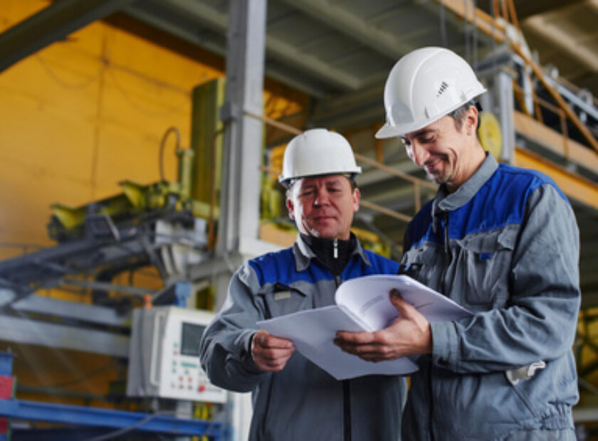 Two workers in overalls holding documents and looking at them in the premises of the factory