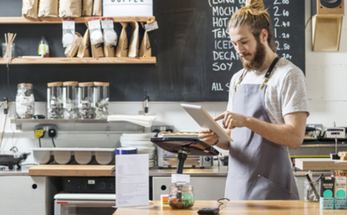 young man behind a counter in a cafe using a tablet