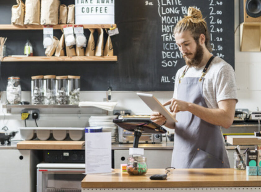young man behind a counter in a cafe using a tablet
